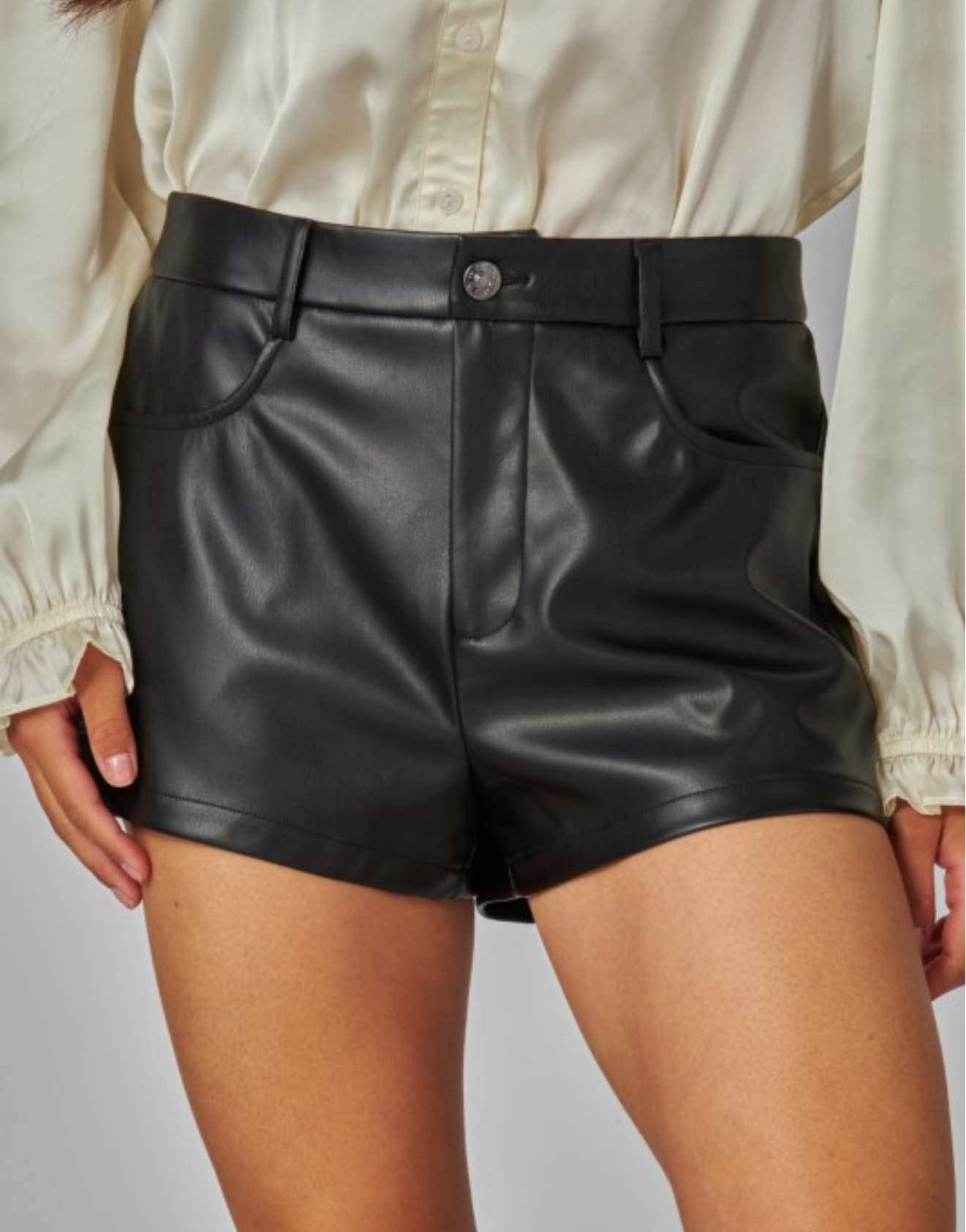 Person wearing black faux leather high-rise shorts on a gray background